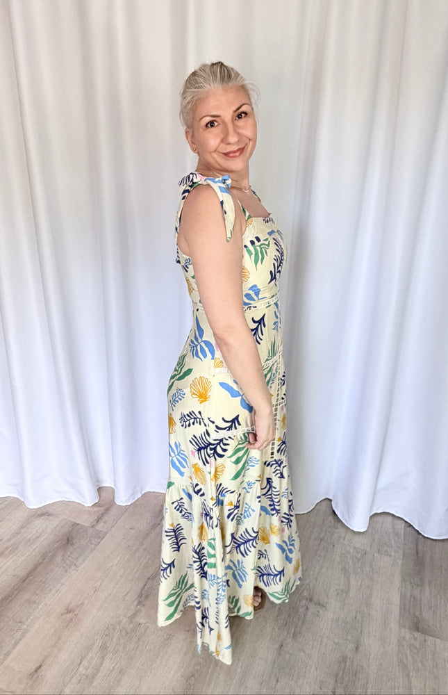 Side profile shot of the reef print maxi dress, emphasizing the clean fit of the upper bodice, the adjustable shoulder ties, and the graceful silhouette of the long tiered skirt.