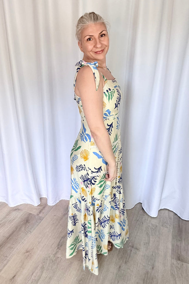 Side profile shot of the reef print maxi dress, emphasizing the clean fit of the upper bodice, the adjustable shoulder ties, and the graceful silhouette of the long tiered skirt.