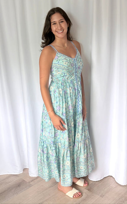 A side view of the model gently holding out the front or back of the skirt, showing the depth, volume, and full pattern layout of the border print from the side.
