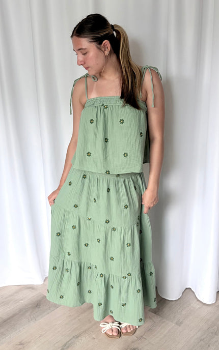 Model wearing a romantic floral embroidered cotton gauze matching set styled for summer, featuring a tiered midi skirt and tie-shoulder tank