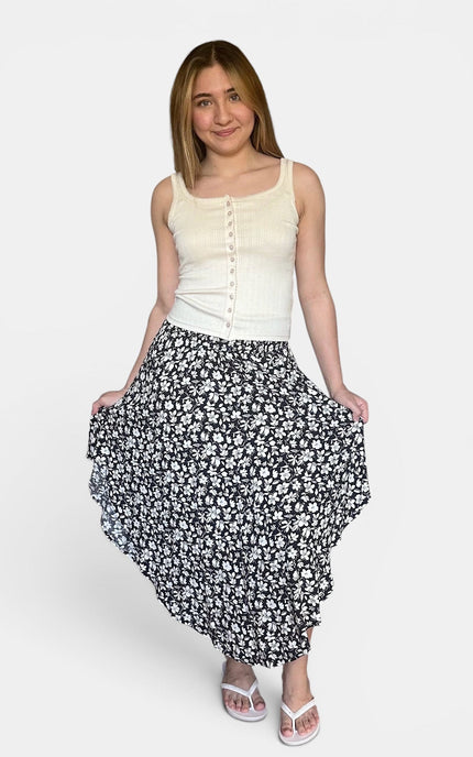 A woman modeling a sleeveless cream button-front top and a black midi skirt with a white floral pattern, standing against a light gray studio background.