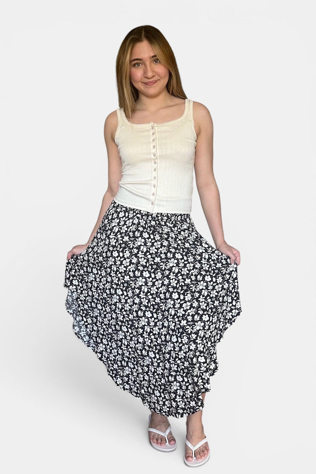A woman modeling a sleeveless cream button-front top and a black midi skirt with a white floral pattern, standing against a light gray studio background.