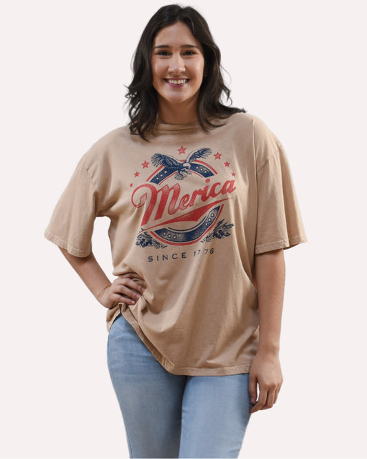 Woman wearing a beige t-shirt with 'Merica' graphic design on a white background
