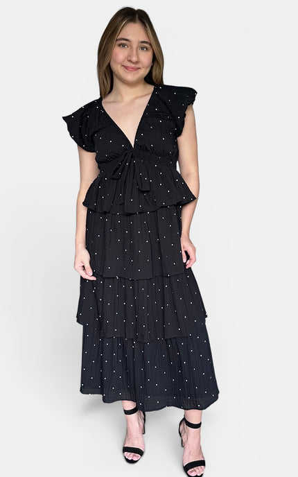 Black cotton tiered maxi dress with white polka dots, ruffled cap sleeves, and a tie-front waist, photographed against a plain light gray studio background.