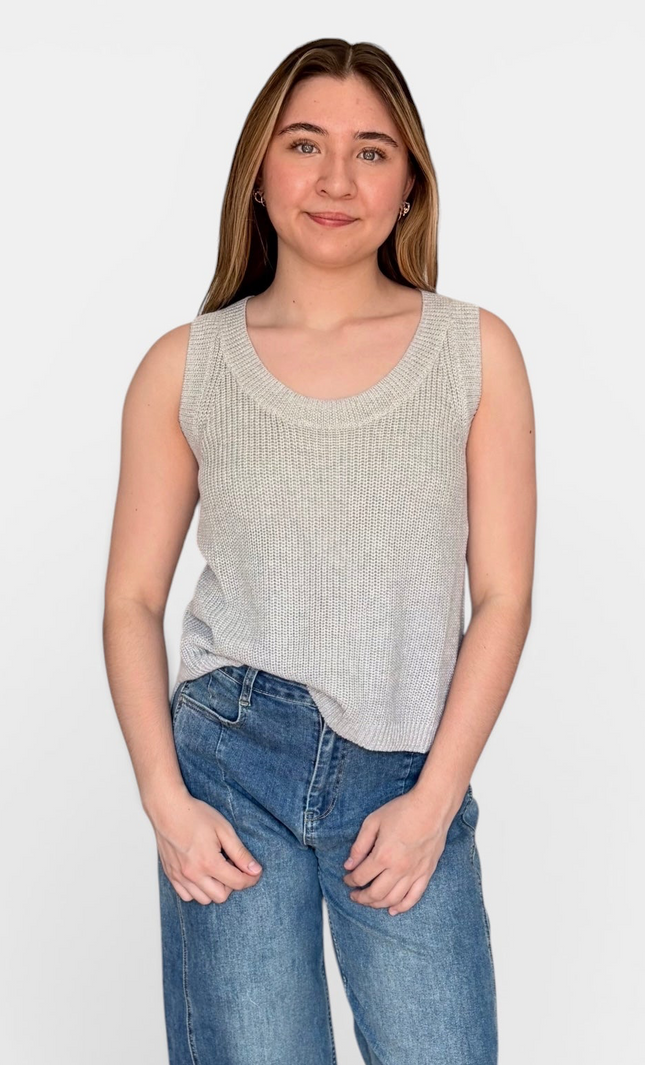 A woman modeling a light gray ribbed knit sleeveless scoop-neck tank top with blue jeans, standing against a plain white studio background.