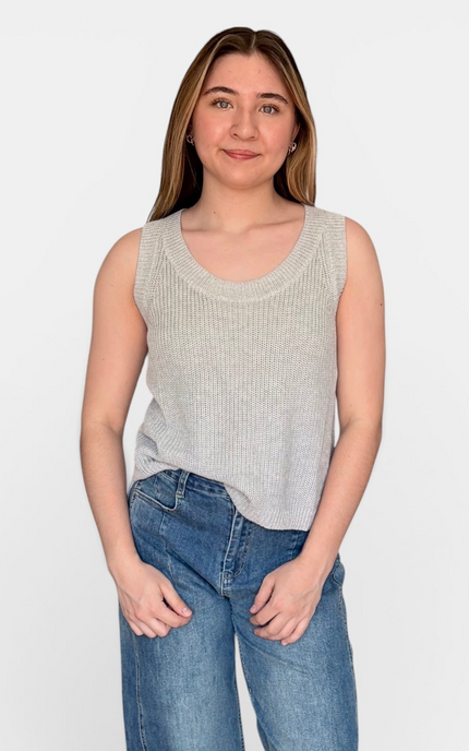 A woman modeling a light gray ribbed knit sleeveless scoop-neck tank top with blue jeans, standing against a plain white studio background.