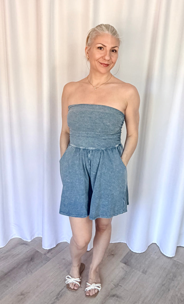 Woman wearing a strapless denim romper against a white curtain background