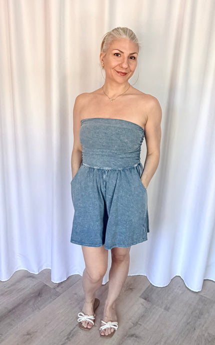 Woman wearing a strapless denim romper against a white curtain background