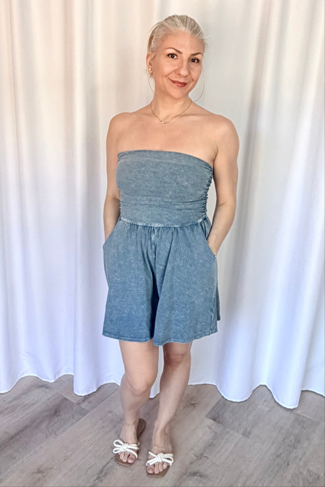 Woman wearing a strapless denim romper against a white curtain background
