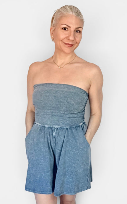 A woman modeling a strapless blue denim romper against a plain light gray background.