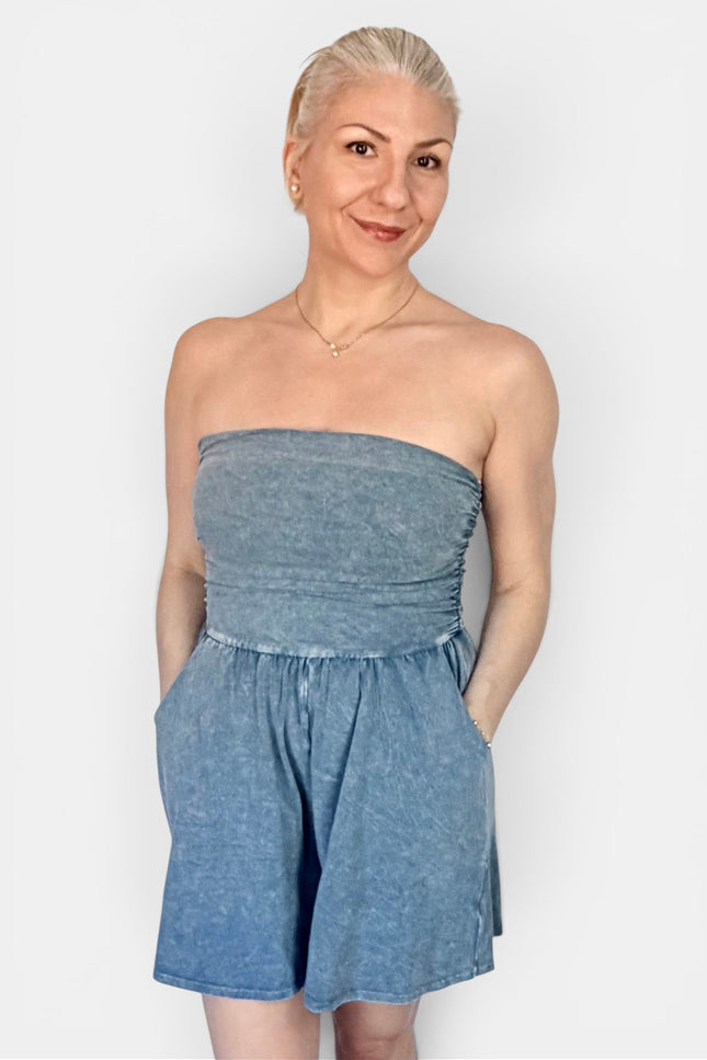 A woman modeling a strapless blue denim romper against a plain light gray background.
