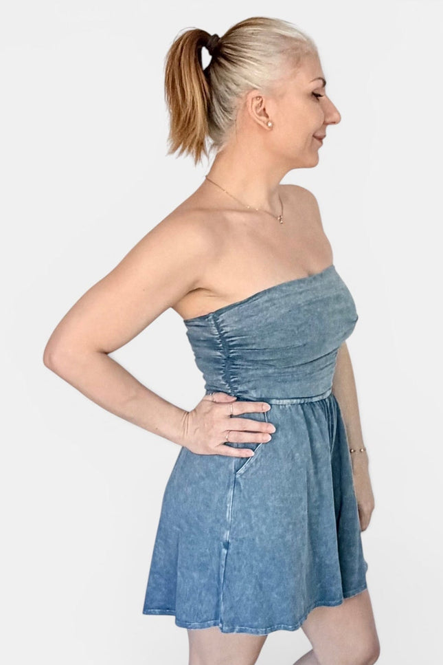 A woman modeling a strapless blue denim mini dress with a gathered bodice and flared skirt, shown in profile against a light gray studio background.