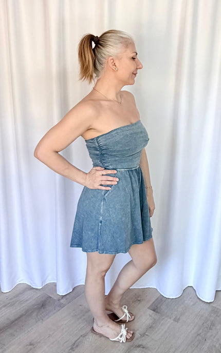 Woman wearing a strapless denim dress against a white curtain background