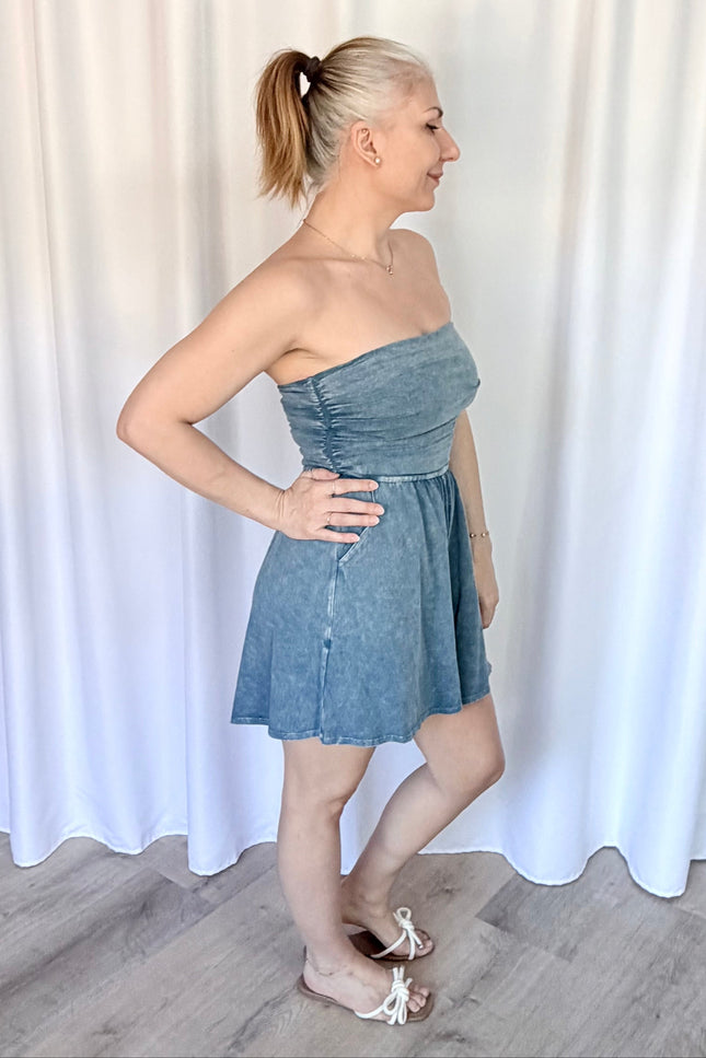 Woman wearing a strapless denim dress against a white curtain background