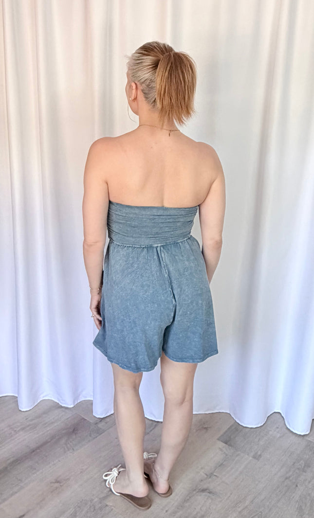 Woman wearing a strapless denim romper against a white curtain background