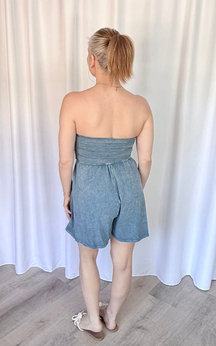 Woman wearing a strapless denim romper against a white curtain background