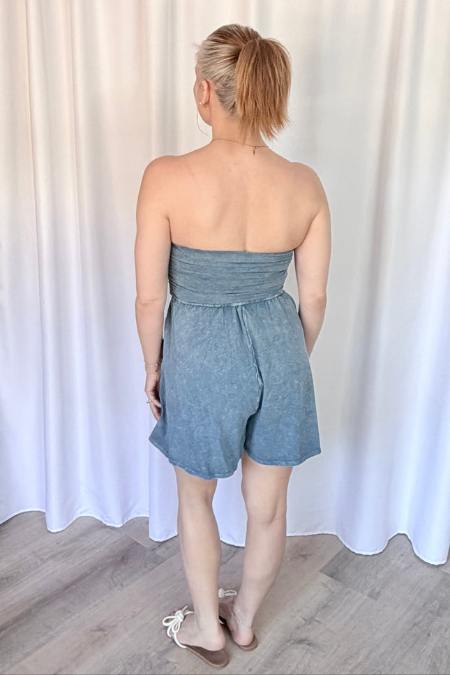 Woman wearing a strapless denim romper against a white curtain background