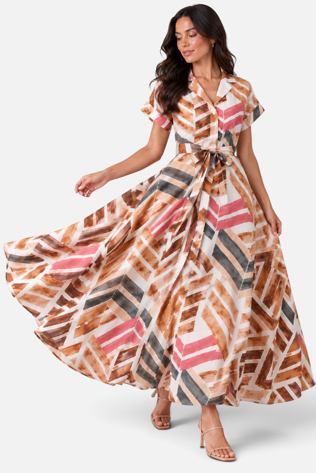 A woman modeling a maxi dress with a geometric brushstroke pattern in brown, pink, gray, and white, posed against a light gray studio background.
