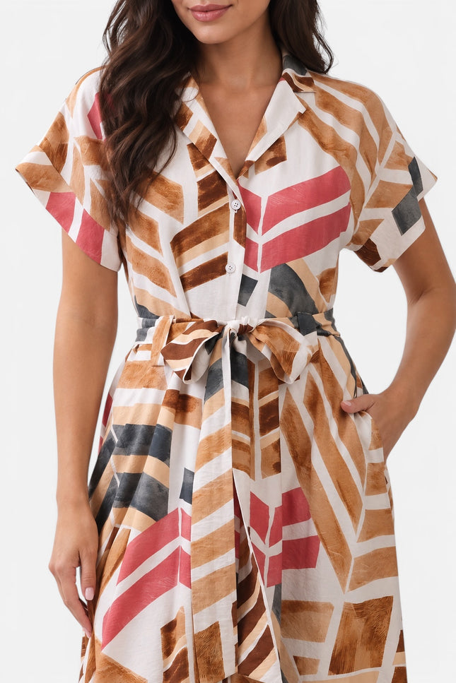 A woman wearing a short-sleeve collared shirt dress with a geometric pattern in brown, pink, black, and white, featuring a tie waist belt.