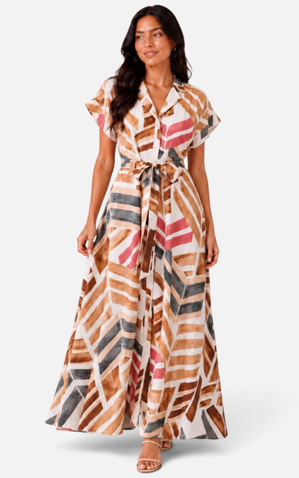 A woman modeling a long maxi dress with a geometric abstract print in brown, beige, pink, and gray on a white background.