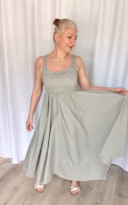 Front view of a model playfully swishing the hem of the gingham Nora Maxi Dress to one side, capturing the lightweight drape and full, airy volume of the 100% cotton skirt.