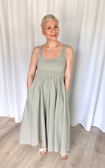 Front view of a model wearing the full-length Nora Maxi Dress in a classic gingham print, showcasing its fitted bodice, wide shoulder straps, and a gathered waist seam that flows into a long, voluminous skirt.