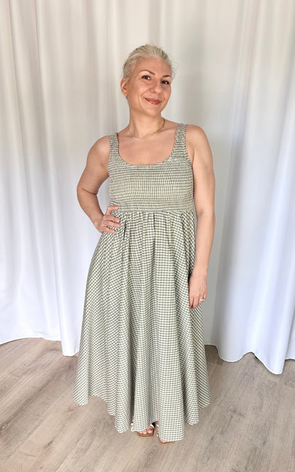 Front view of a model wearing the full-length Nora Maxi Dress in a classic gingham print, showcasing its fitted bodice, wide shoulder straps, and a gathered waist seam that flows into a long, voluminous skirt.