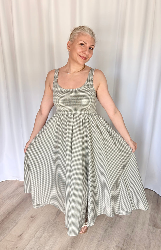 Front view of a model lightly holding the fabric of the gingham Nora Maxi Dress at each side, flaring the skirt outward to display its full, voluminous width and the graceful drape of the breathable cotton.