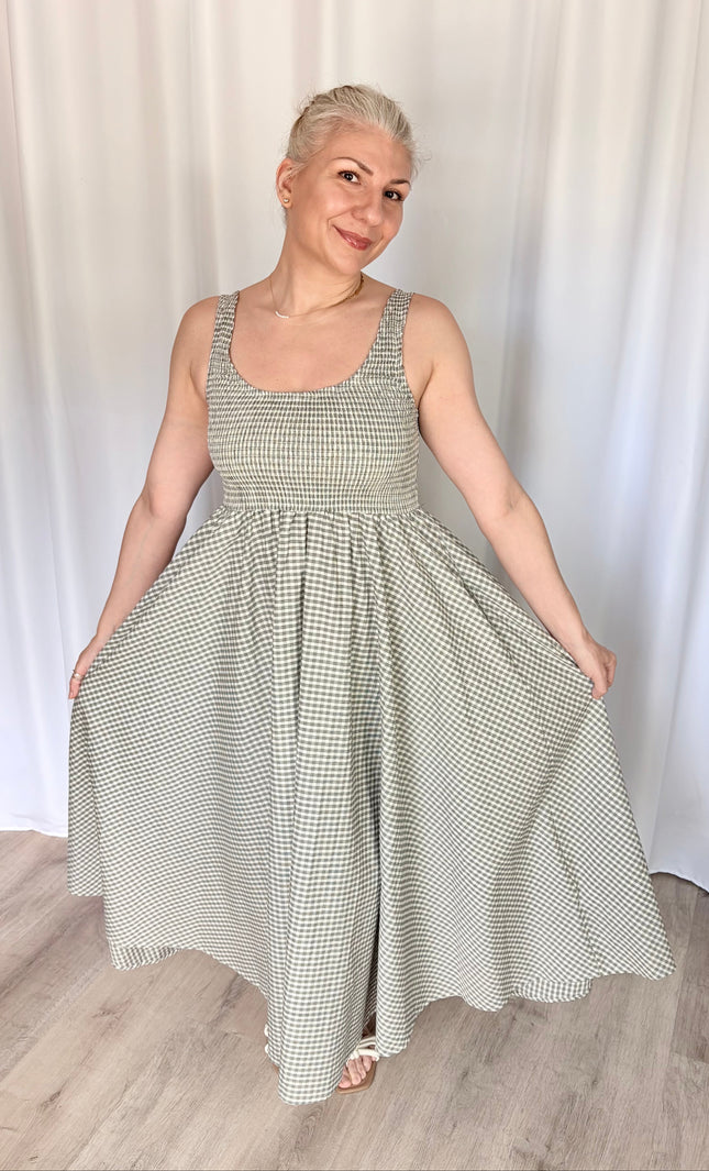 Front view of a model lightly holding the fabric of the gingham Nora Maxi Dress at each side, flaring the skirt outward to display its full, voluminous width and the graceful drape of the breathable cotton.