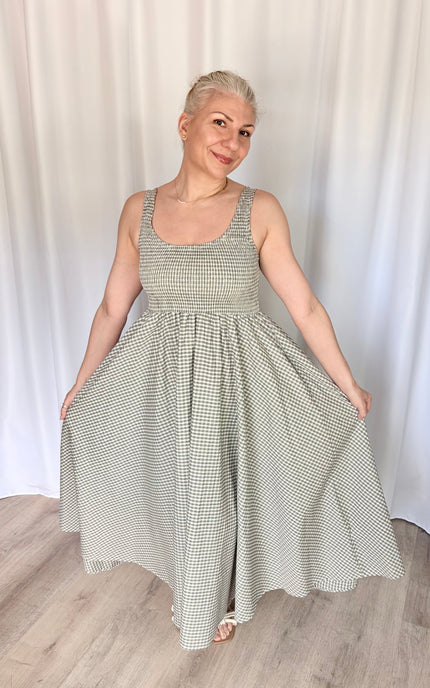 Front view of a model lightly holding the fabric of the gingham Nora Maxi Dress at each side, flaring the skirt outward to display its full, voluminous width and the graceful drape of the breathable cotton.