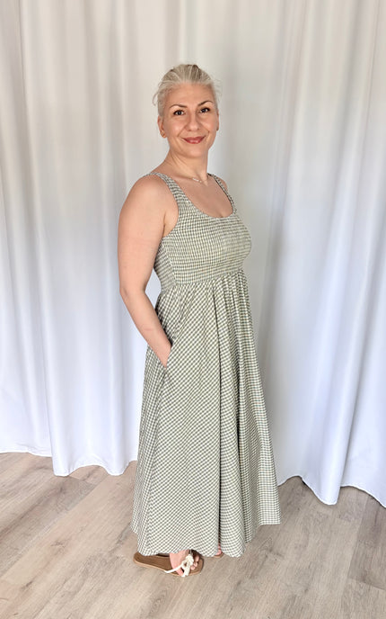 A side profile shot of a model with one hand resting naturally inside the functional side pocket of the gingham Nora Maxi Dress, highlighting the seamless integration of the pocket and the clean line of the waist-defining silhouette.