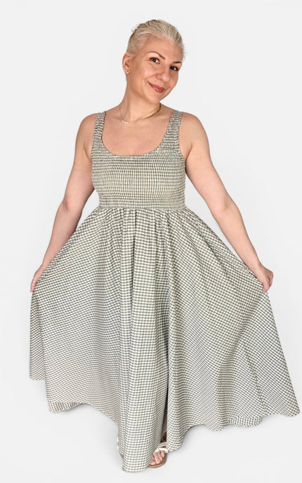 A woman modeling a sleeveless, scoop-neck maxi dress with a small-scale black and white gingham pattern, set against a solid light gray background.