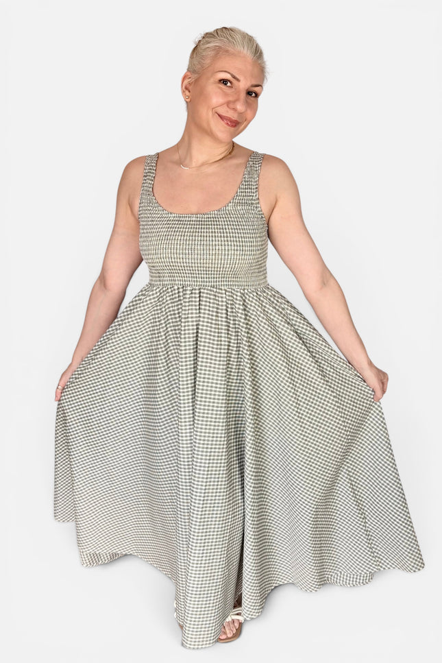 A woman modeling a sleeveless, scoop-neck maxi dress with a small-scale black and white gingham pattern, set against a solid light gray background.