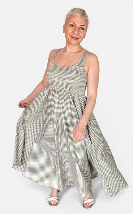 An older woman modeling a sleeveless, scoop-neck maxi dress with a small-scale black and white gingham pattern, standing against a solid light gray background.
