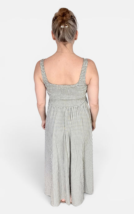 A woman viewed from behind wearing a sleeveless smocked maxi dress with a small black and white gingham pattern, set against a plain light gray studio background.
