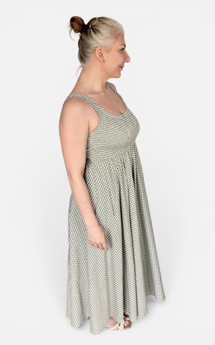 A woman modeling a sleeveless, scoop-neck maxi dress with a small-scale green and white geometric pattern, shown from a side profile against a plain light gray studio background.
