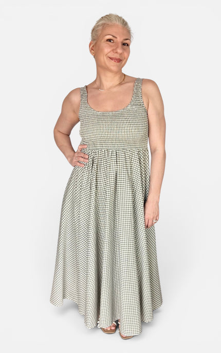 A woman modeling a sleeveless, scoop-neck maxi dress with a green and beige gingham pattern, standing against a light gray studio background.