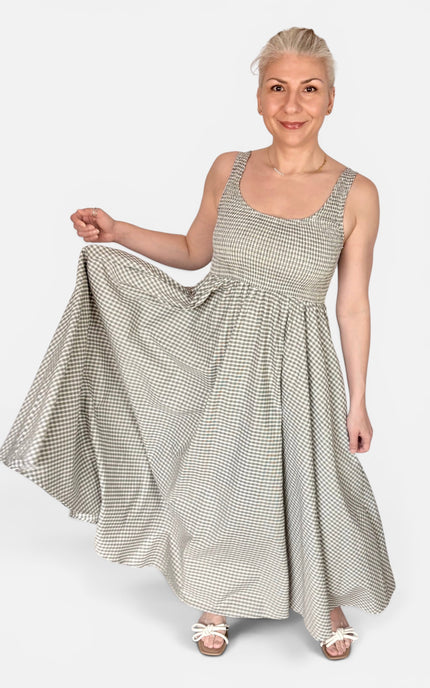 A woman modeling a sleeveless, scoop-neck maxi dress with a small-scale black and white gingham pattern, holding out the skirt to show its volume against a light gray studio background.