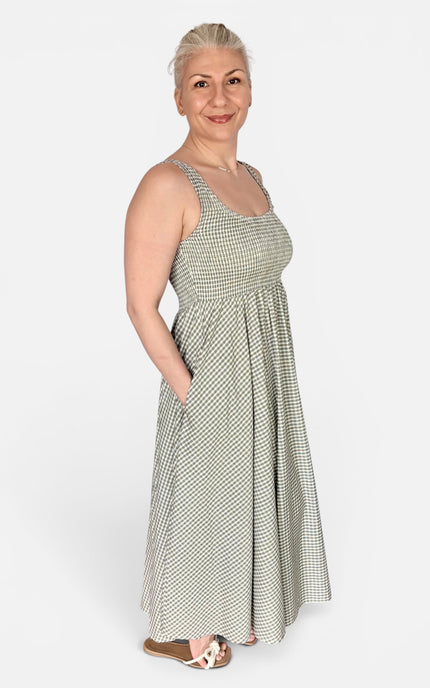 A woman modeling a sleeveless, scoop-neck maxi dress with a small green and white gingham pattern, standing against a plain light gray studio background.