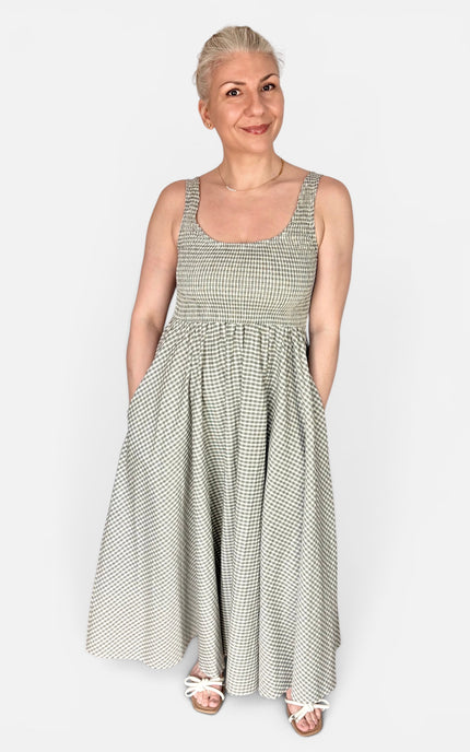 A woman modeling a sleeveless, scoop-neck maxi dress with a small gray and white gingham pattern, standing against a light gray studio background.