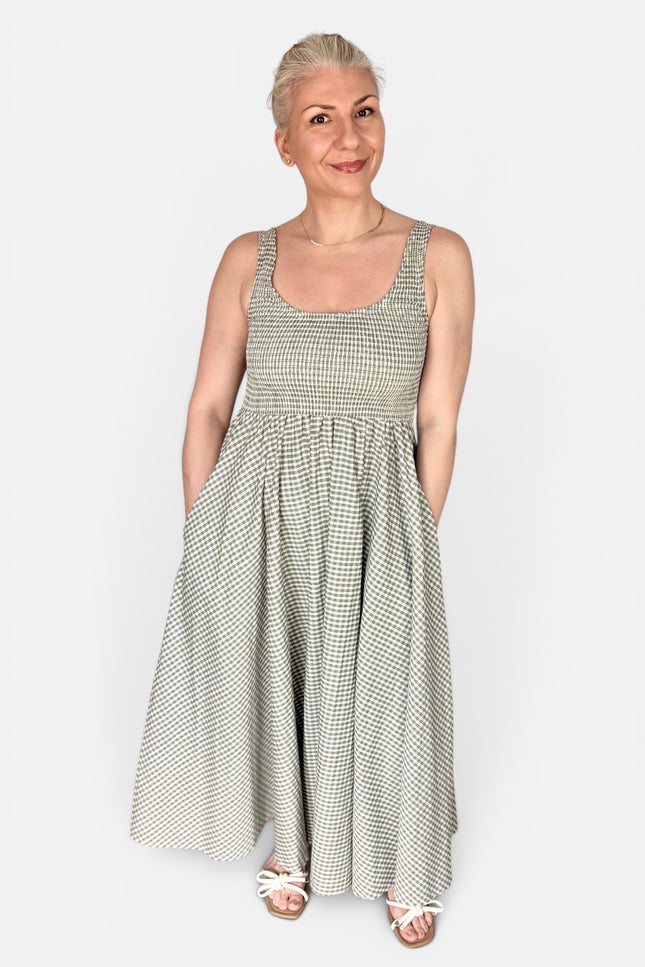 A woman modeling a sleeveless, scoop-neck maxi dress with a small gray and white gingham pattern, standing against a light gray studio background.
