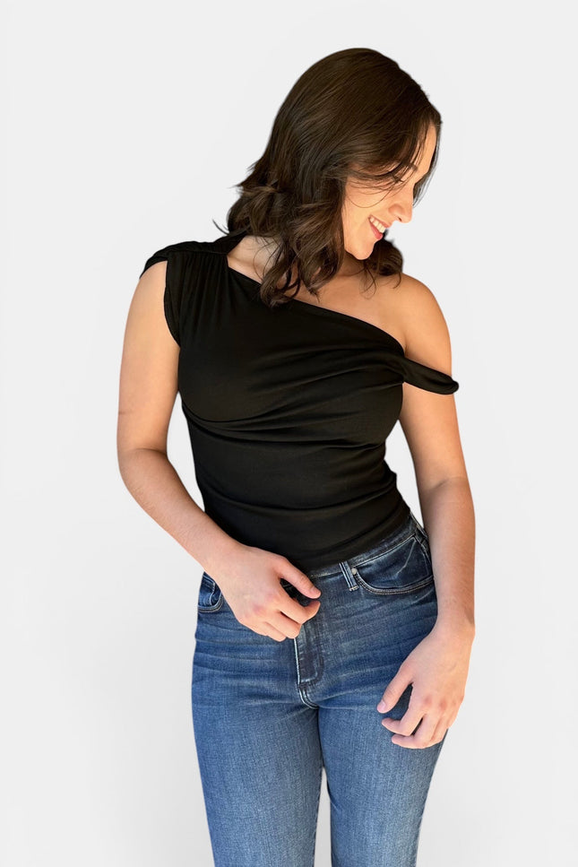 Woman wearing a black asymmetrical off shoulder twist front fitted knit top with denim jeans.
