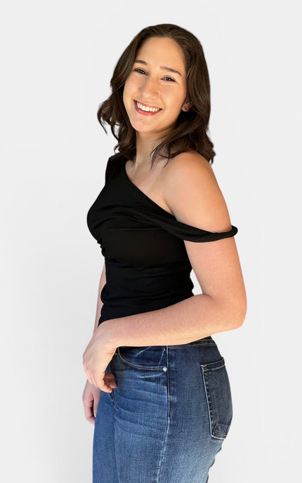 Modern black off shoulder asymmetrical top with twist detail paired with blue jeans for a chic casual outfit.