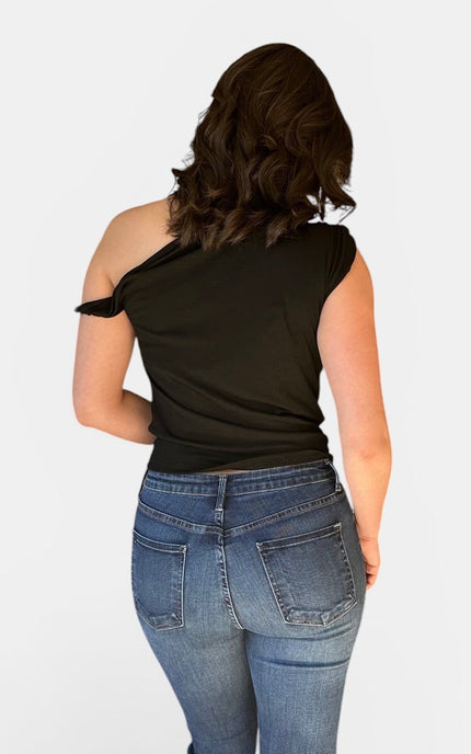 Back view of black off shoulder asymmetrical top with twist detail paired with blue jeans for a chic casual outfit.