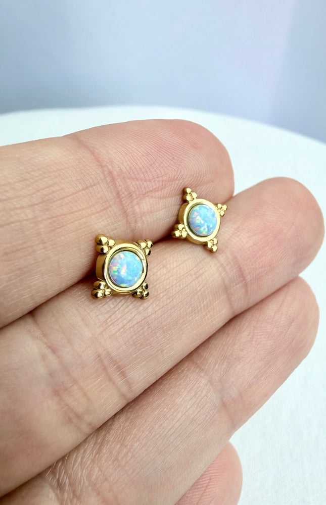 Gold earrings with opal stones held between fingers on a light background