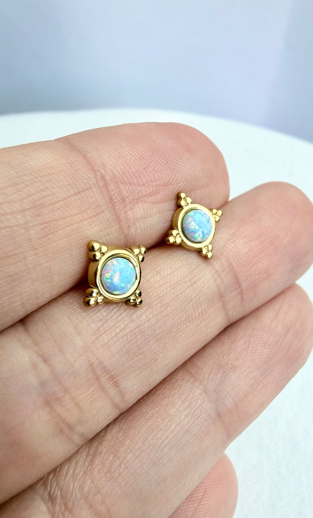 Gold earrings with opal stones held between fingers on a light background