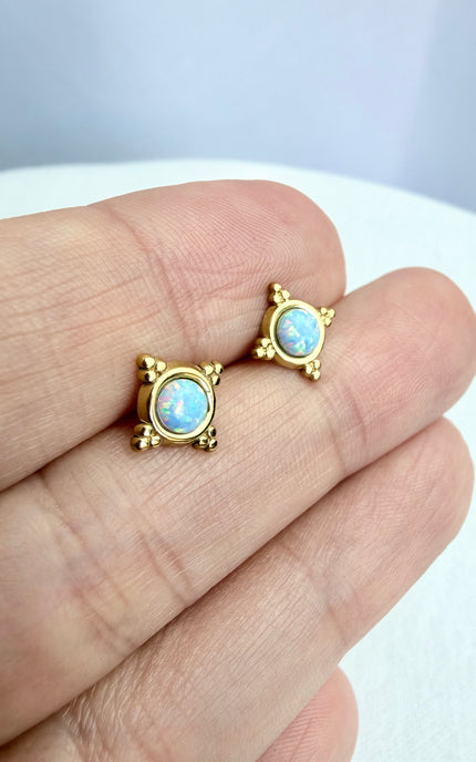Gold earrings with opal stones held between fingers on a light background