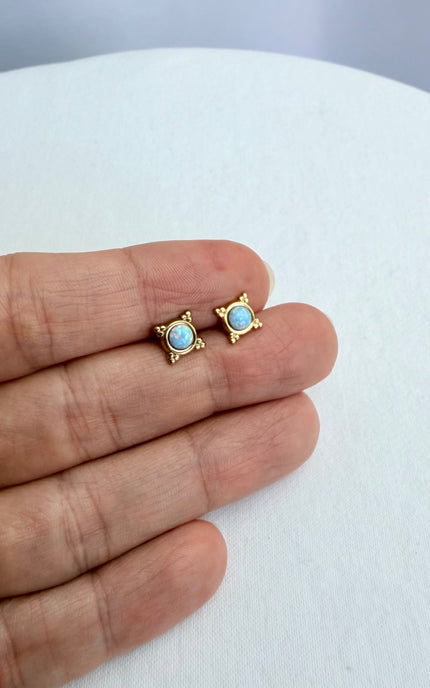 Gold earrings with turquoise stones held between fingers on a white background