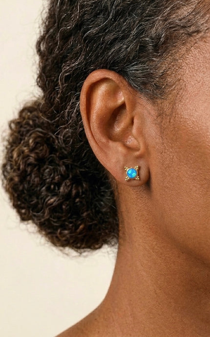 Close-up of an ear wearing a gold earring with a blue gemstone on a beige background