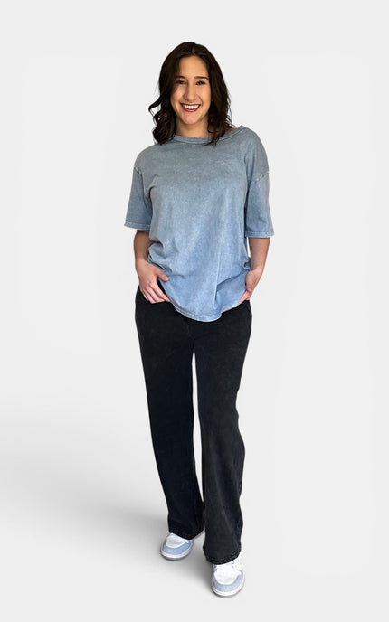 A woman modeling a light blue heathered short-sleeve t-shirt and black wide-leg pants against a light gray studio background.